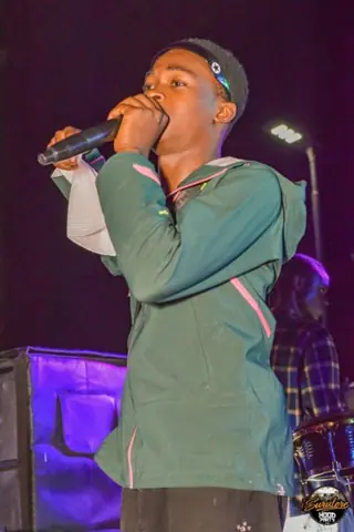 A singer in a green shirt performing into a microphone